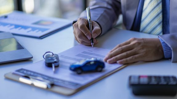 auto insurance agent writing up an auto insurance policy on his desk. Auto insurance essentials policy owners should know.