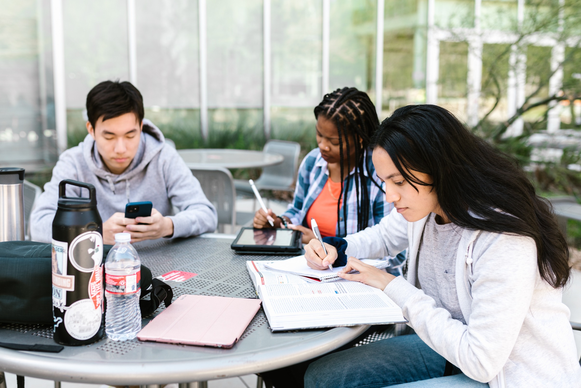 three post-secondary students sitting at a round table outside and studying.