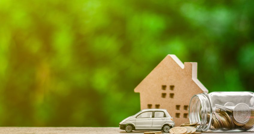 Mini house and car, and a tipped over jar of coins over a blurred background