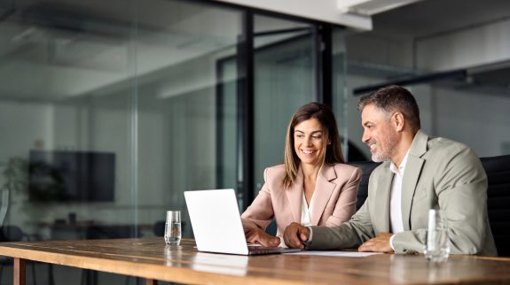 A man and woman sitting at a table and looking at a laptop