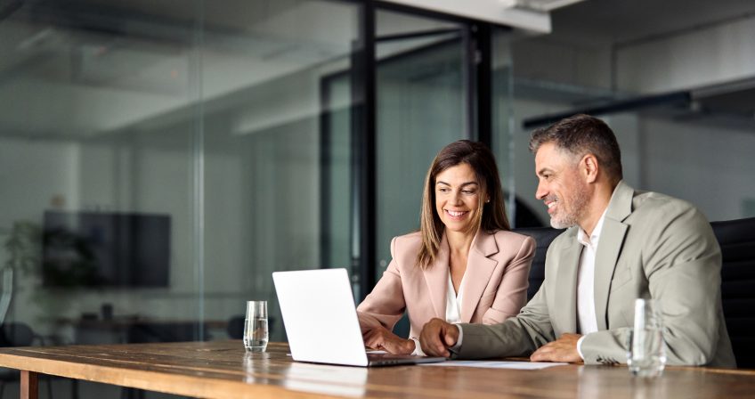A man and woman sitting at a table and looking at a laptop
