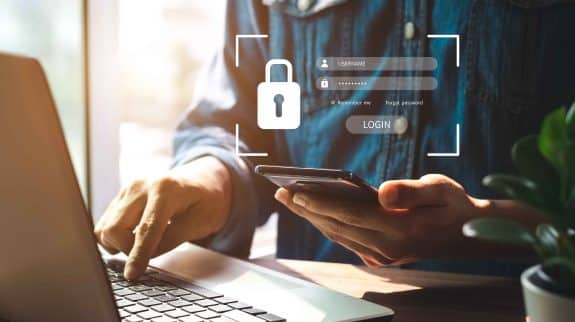A person using a laptop and smartphone to complete a secure login with multi-factor authentication, representing cybersecurity and data protection.