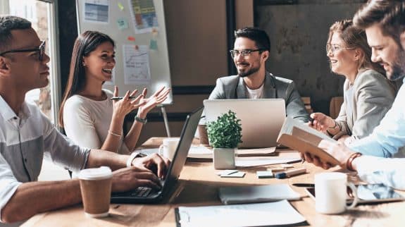 Business team collaborating during a meeting in a modern office with laptops, documents, and a whiteboard.