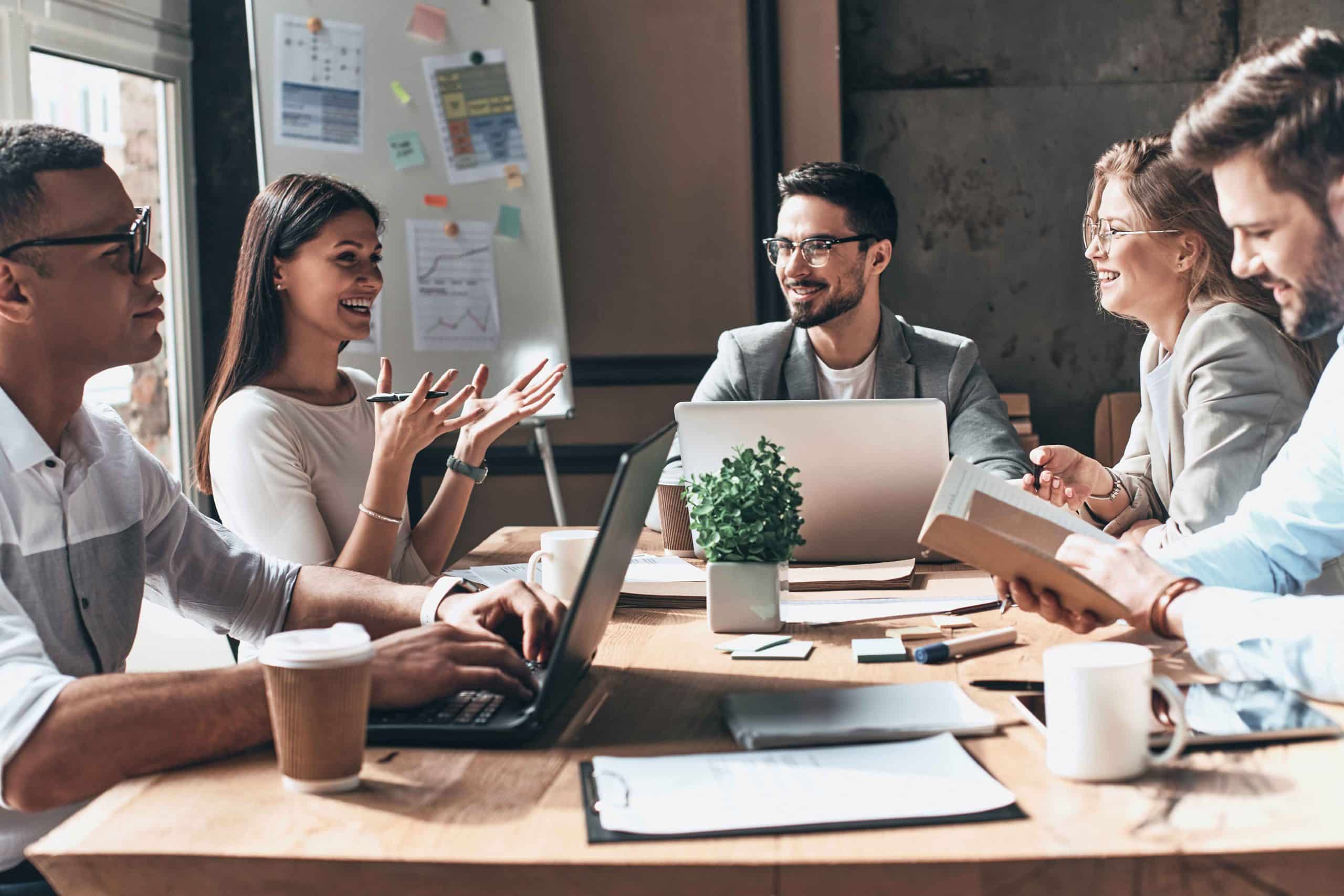 Business team collaborating during a meeting in a modern office with laptops, documents, and a whiteboard.