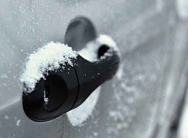 Frozen car door handle covered in snow during icy winter conditions