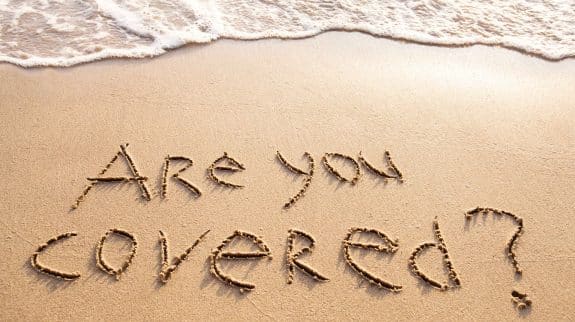 Are you covered written in the sand on a beach, symbolizing the importance of travel insurance coverage and vacation protection