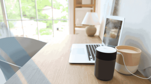 Minimalist home office desk setup with laptop, coffee mug, smart speaker, and natural window light