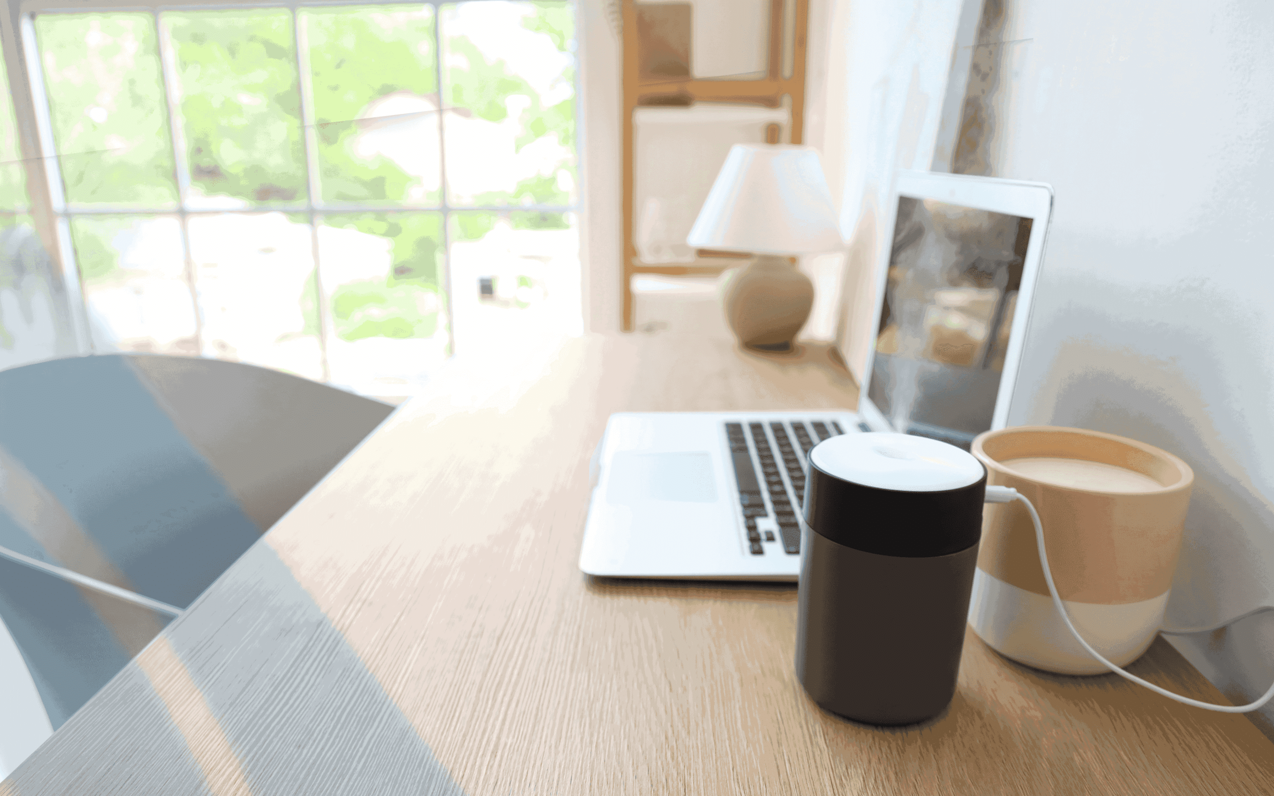 Minimalist home office desk setup with laptop, coffee mug, smart speaker, and natural window light