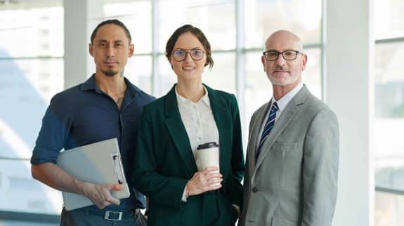 Three diverse business professionals standing together in a modern office, representing leadership, teamwork, and corporate success.