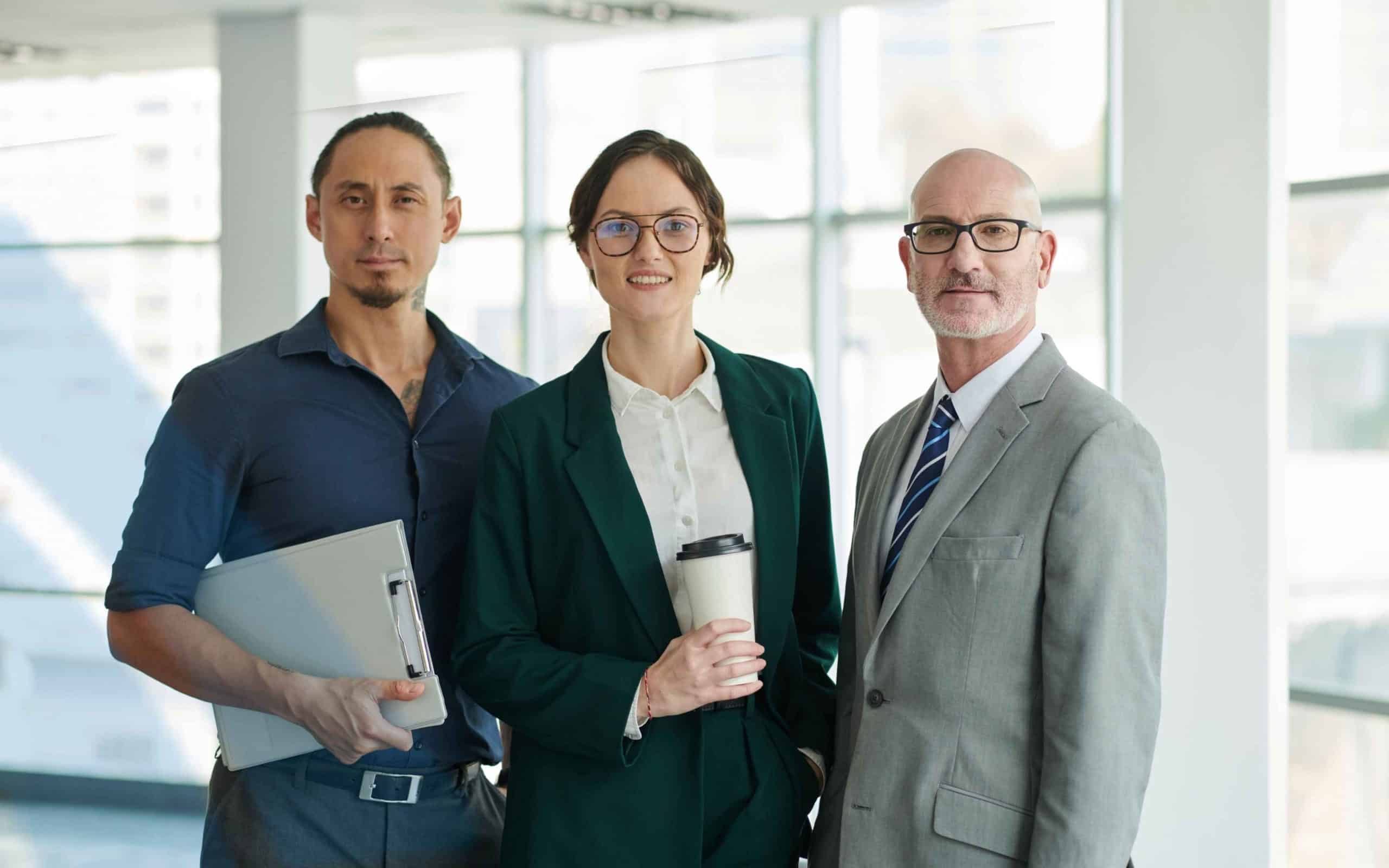 Three diverse business professionals standing together in a modern office, representing leadership, teamwork, and corporate success.