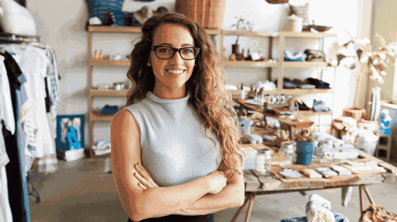 Female small business owner standing in a handmade craft studio surrounded by artisan products and creative workspace materials.