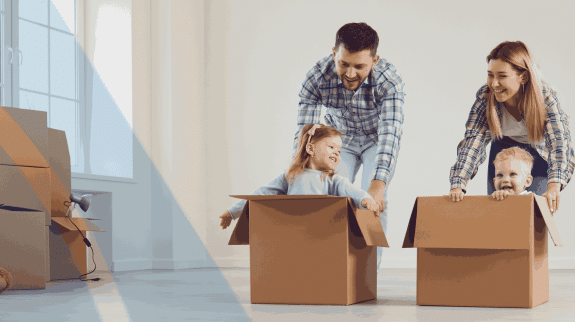 Young family with two children playing in cardboard moving boxes while unpacking in a new home during relocation.