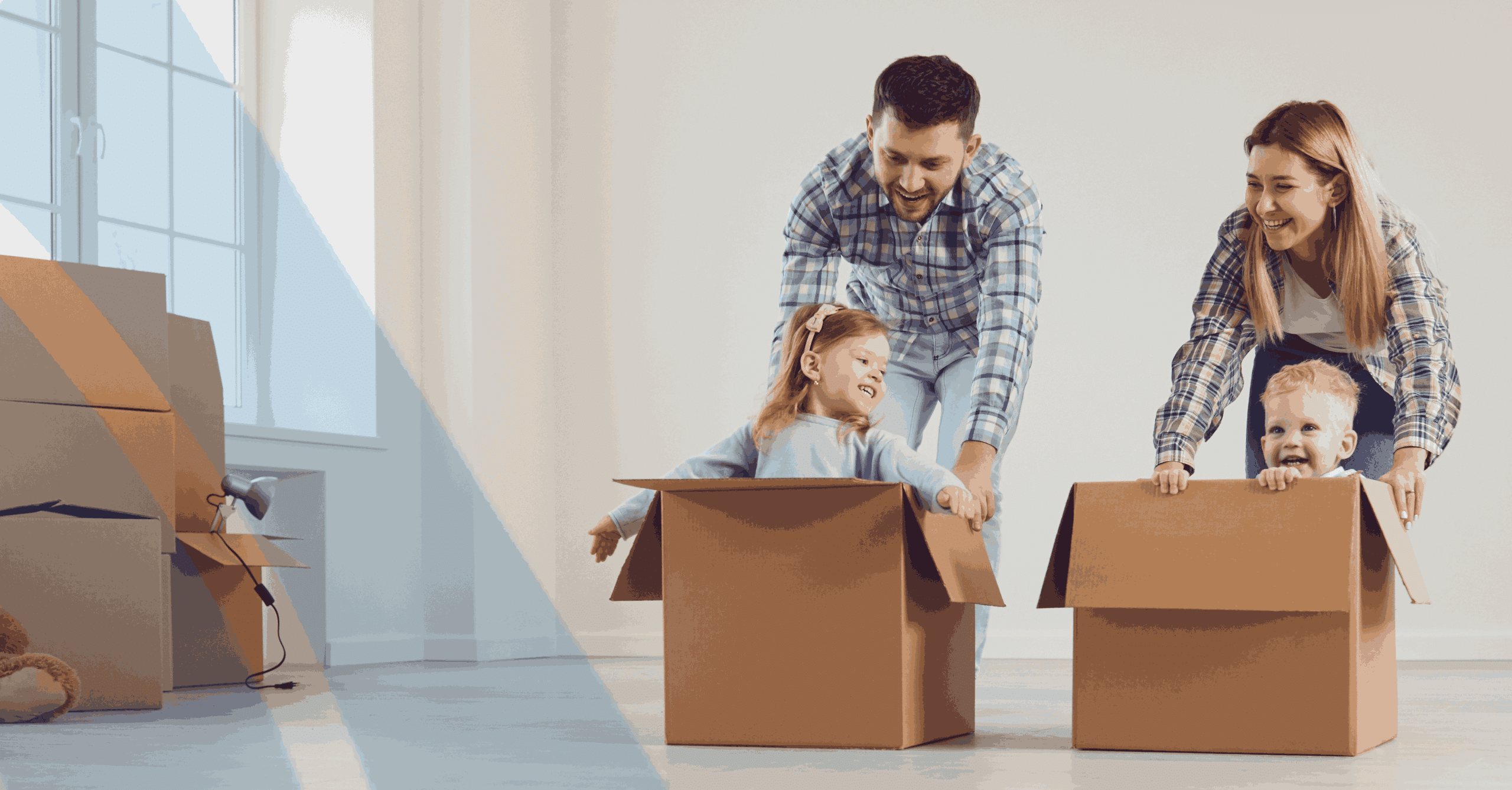 Young family with two children playing in cardboard moving boxes while unpacking in a new home during relocation.