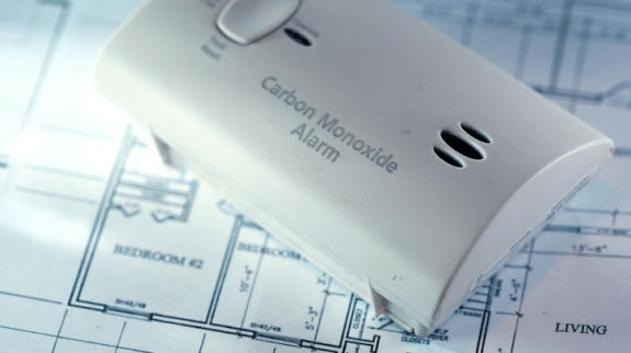 Carbon monoxide alarm placed on a residential house floor plan blueprint, illustrating home safety planning and indoor air protection.