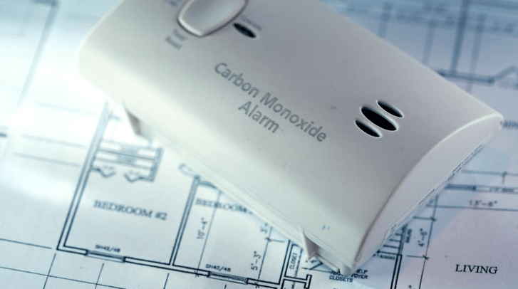 Carbon monoxide alarm placed on a residential house floor plan blueprint, illustrating home safety planning and indoor air protection.