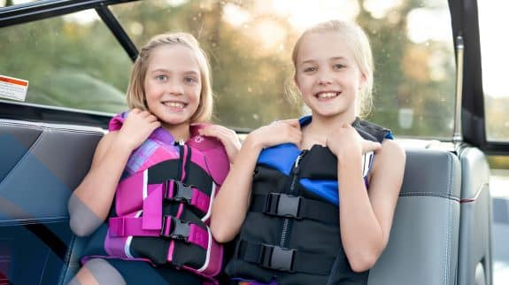 Two passengers seated on a recreational boat wearing secured life jackets, demonstrating essential boating safety practices.