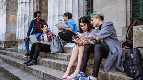 College students studying and using digital devices on a university campus, representing insurance coverage considerations for dependent children attending college.