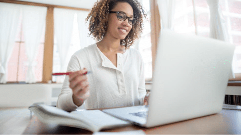 Individual participating in online financial education training on a laptop while taking notes, illustrating employee engagement in workplace financial wellness and learning programs.