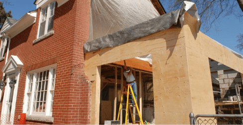 Brick house with a home addition under construction, featuring exposed wooden framing and a worker on a ladder, illustrating the need to update homeowners insurance after major renovations.